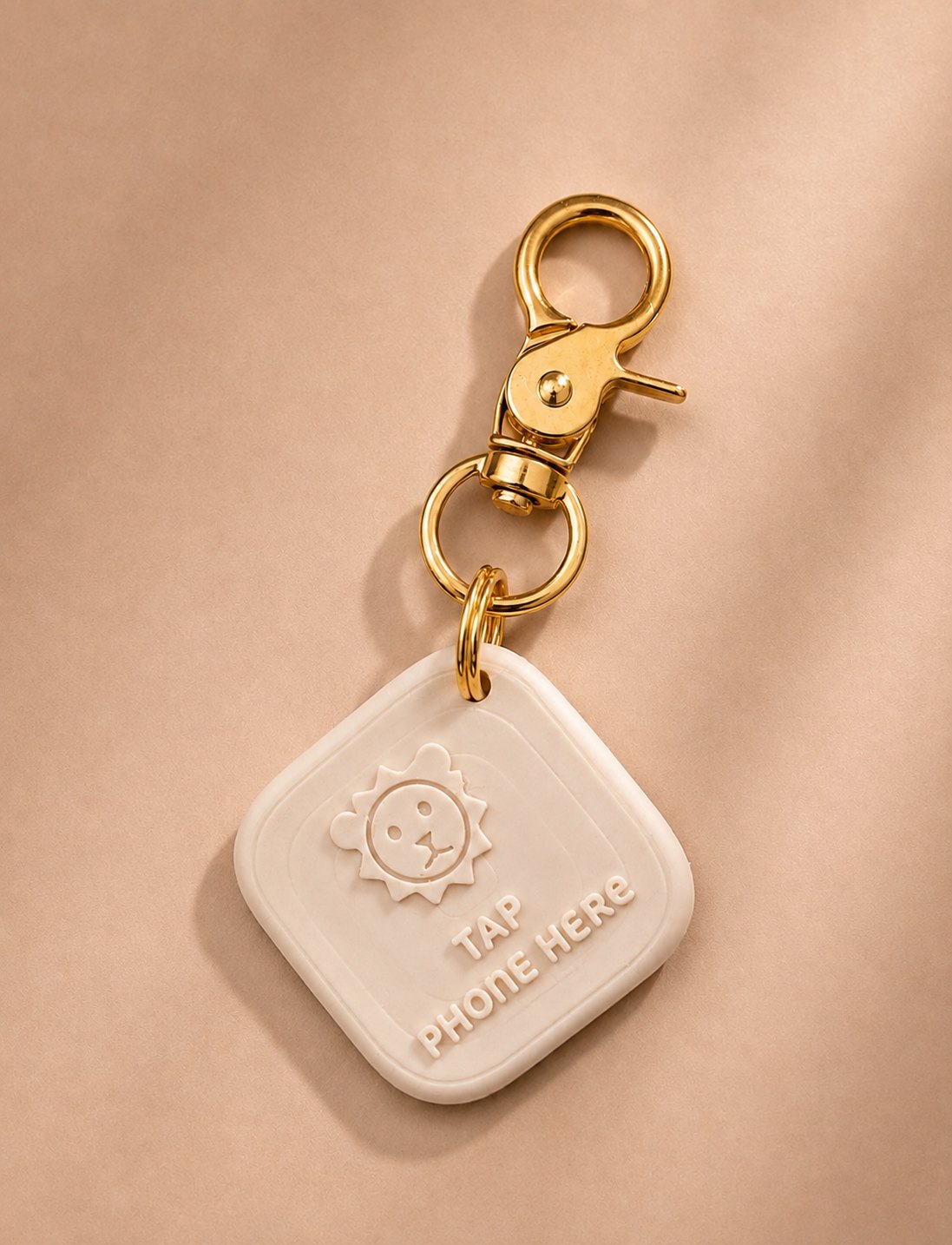Tippi Anhänger in Creme mit Löwenmotiv, Schriftzug Tap phone here und goldenem Karabiner
